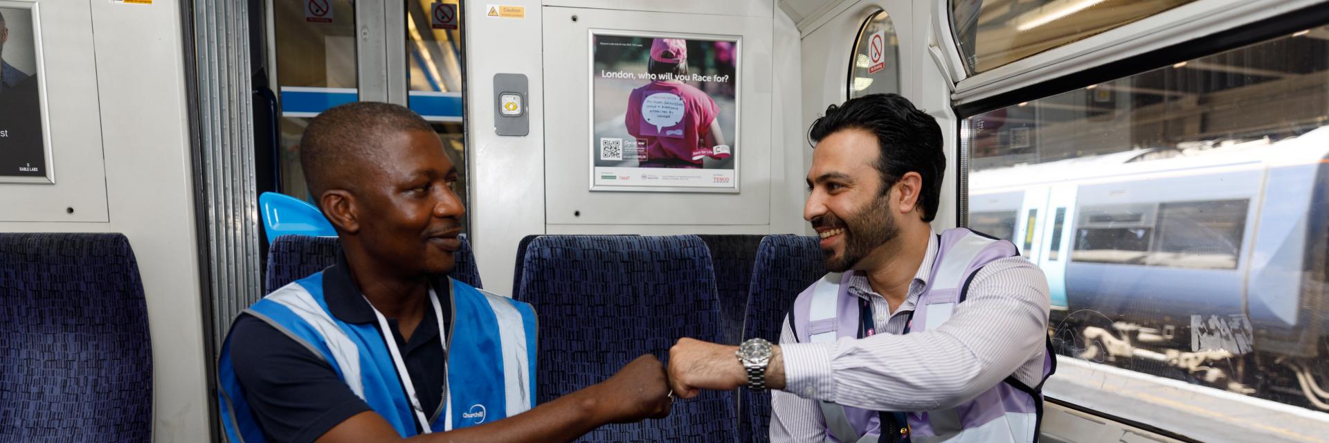 two rail workers sat on a train, fist bumping each other