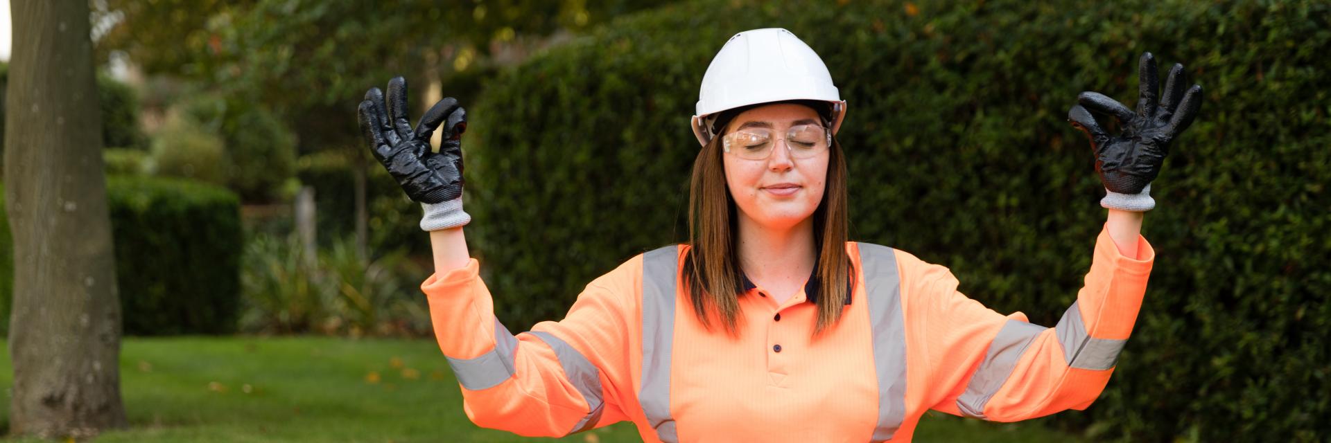 rail worker in orange uniform sat cross legged on some grass, meditating