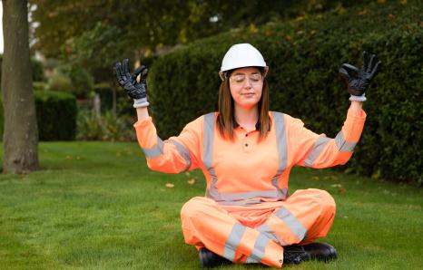 rail worker in orange uniform sat cross legged on some grass, meditating